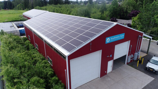 aerial angled view of two structures at Headwaters Farm, including a barn in the foreground and a storage shed in the background, with solar-panel-covered roofs visible on both structures